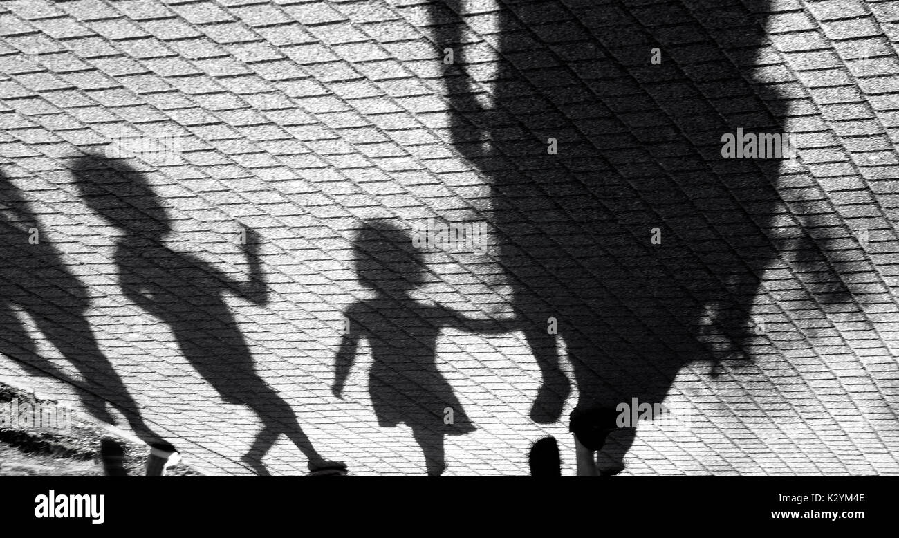 Sfocata ombra di un po' di un ragazzo e una ragazza camminare con gli adulti su park marciapiede in bianco e nero Foto Stock