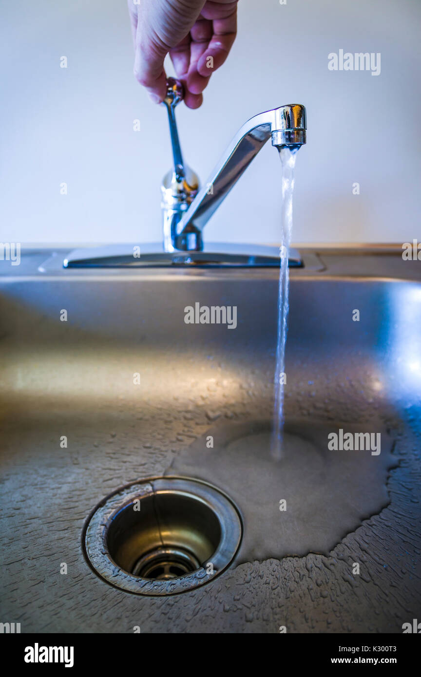 Un basso angolo di visione di una mano girando su un rubinetto di cucina. Foto Stock