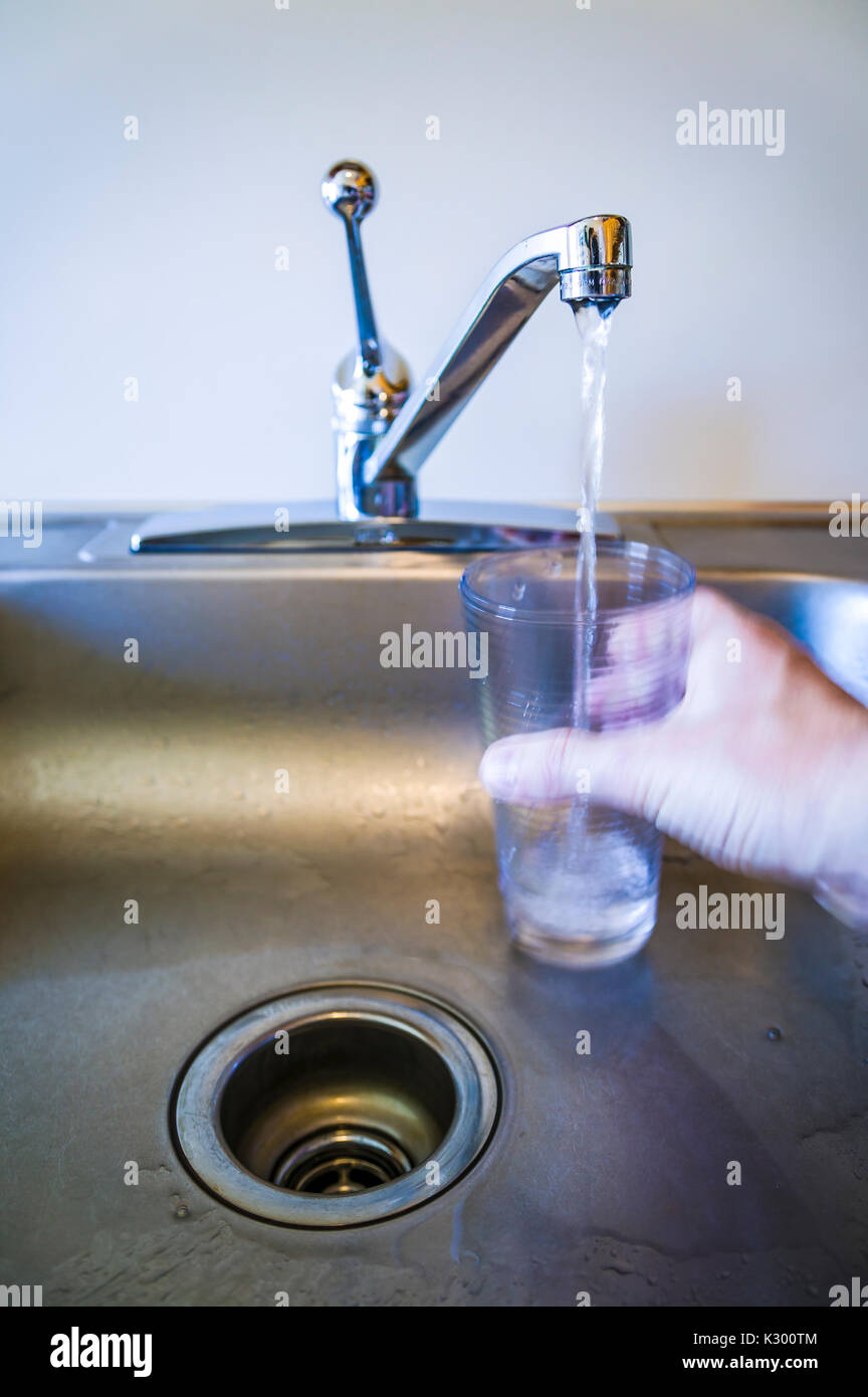 Una mano che tiene un bicchiere al di sotto di un rubinetto che scorre. Foto Stock