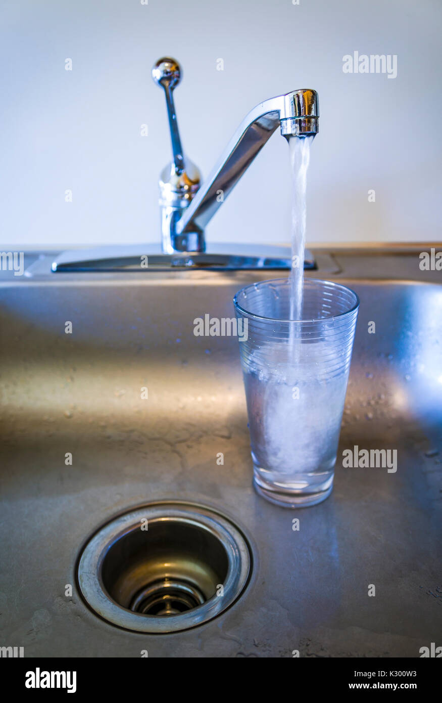 Un basso angolo di visione di un lavello e rubinetto in esecuzione con un bicchiere pieno di acqua. Foto Stock