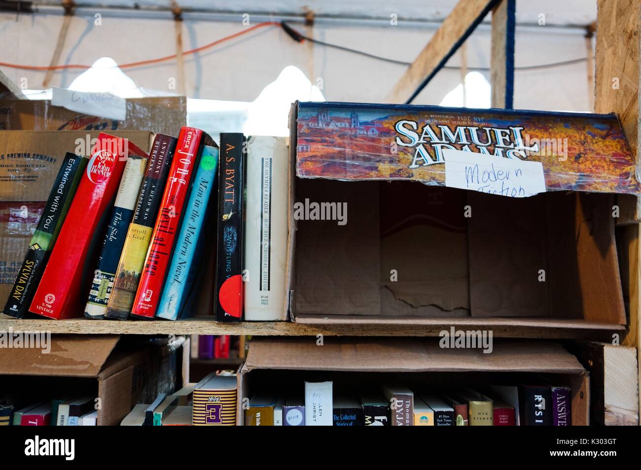 Un ripiano di libri usati in vendita appoggiata contro un vuoto di birra caso, denominata 'Moderne Fiction, ' durante la Baltimore Book Festival, Baltimore, Maryland, Settembre, 2013. Foto Stock