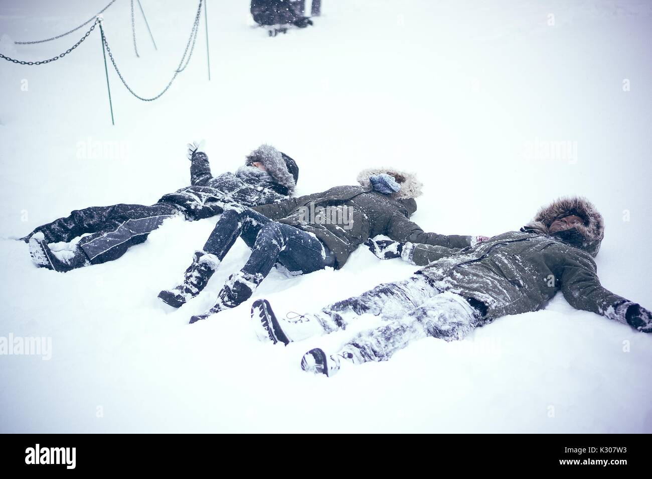 Tre studenti che indossa la neve marcia creare gli angeli di neve a fianco a fianco nella neve, le braccia e le gambe sono aperti a ventaglio verso l'esterno, durante una giornata sulla neve alla Johns Hopkins University, Baltimora, Maryland, 2016. Foto Stock