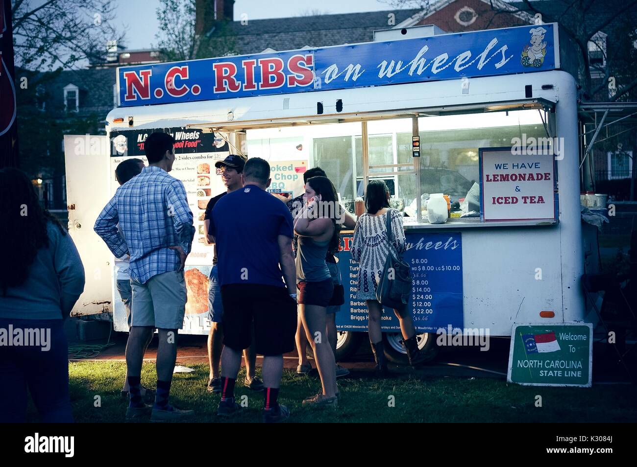 Adulti di conversare mentre in piedi in linea per un 'NC NERVATURE' carrello alimentare al crepuscolo, durante la Fiera di Primavera, uno studente-eseguire il carnevale di primavera presso la Johns Hopkins University, Baltimora, Maryland, aprile 2016. La cortesia Eric Chen. Foto Stock