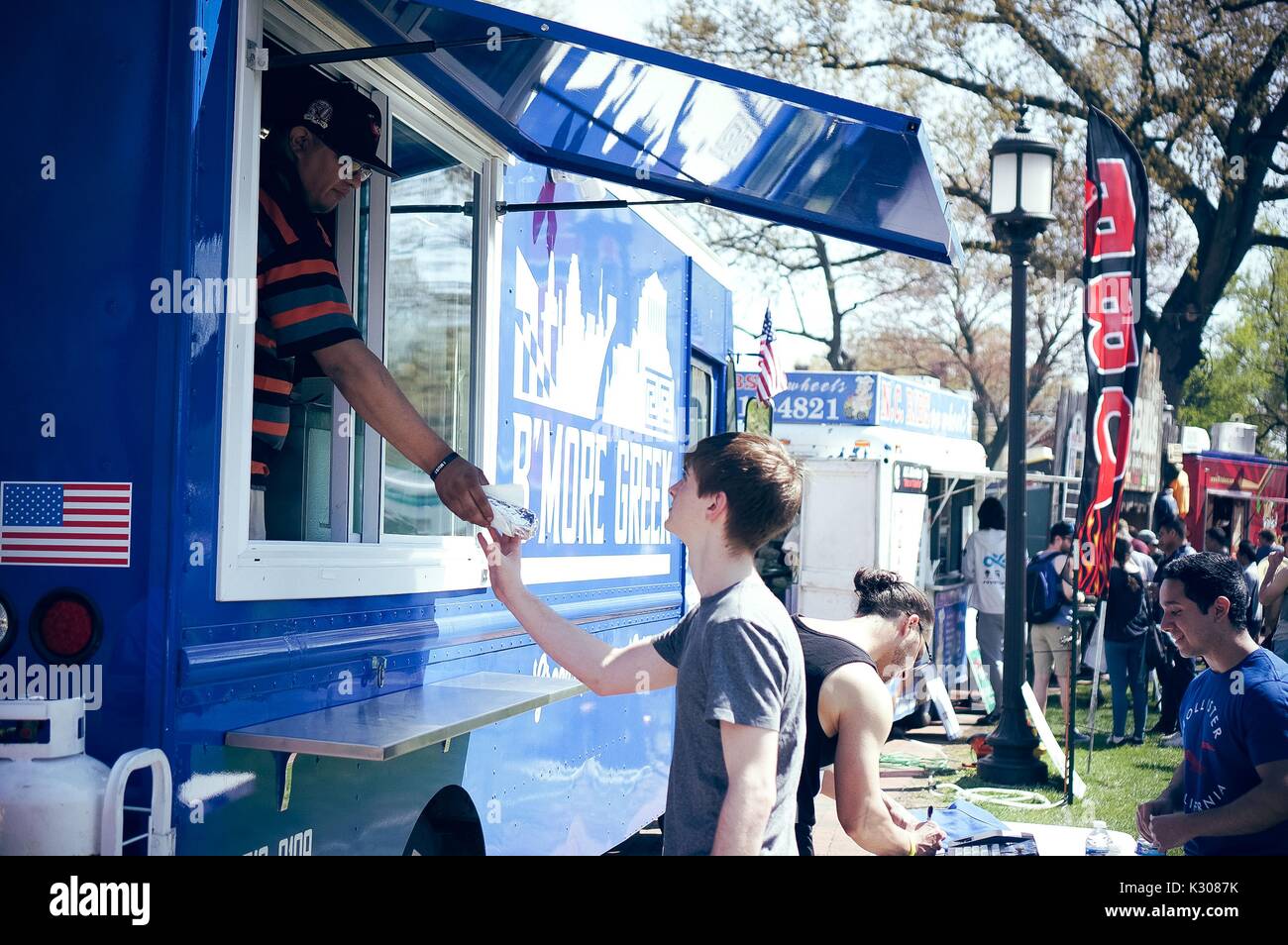 Un uomo dall'interno di un alimento carrello mani un maschio di studente un sandwich avvolti in carta metallizzata, durante la Fiera di Primavera, uno studente-eseguire il carnevale di primavera presso la Johns Hopkins University, Baltimora, Maryland, aprile 2016. La cortesia Eric Chen. Foto Stock