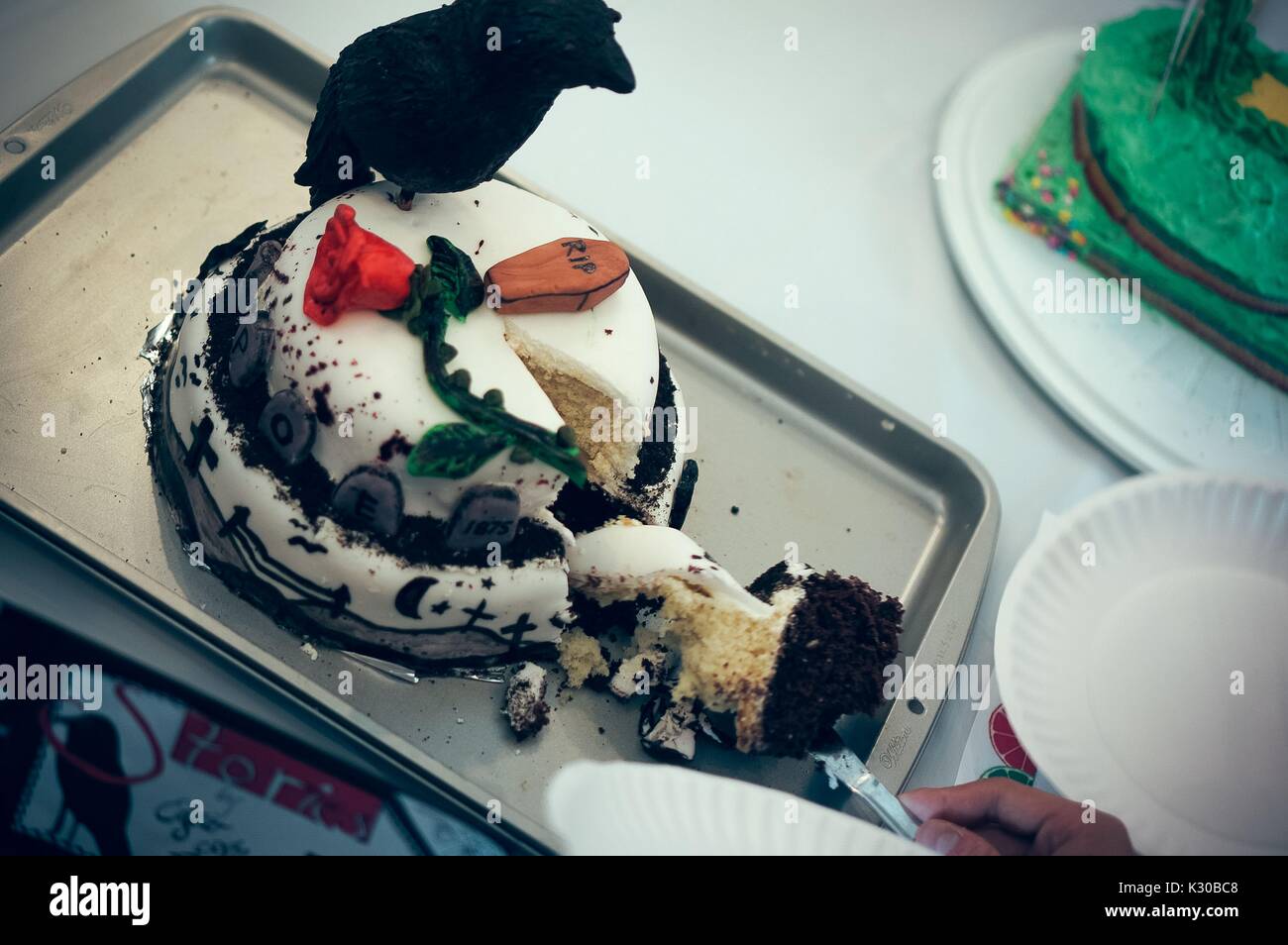 Una lama di taglio di una fetta di torta con una bara, una rosa e un corvo su di essa che rappresenta le storie di Edgar Allan Poe nel libro commestibili Festival presso la Johns Hopkins University, Baltimora, Maryland, Marzo 31, 2016. La cortesia Eric Chen. Foto Stock