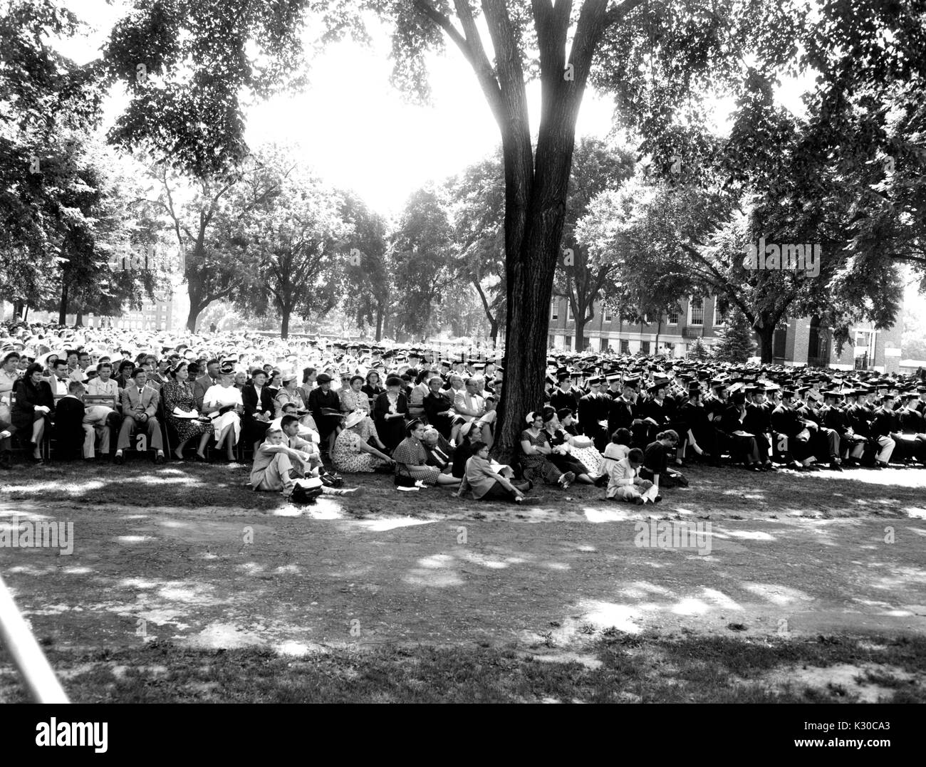 Il giorno d'inizio, centinaia di laureati e le loro famiglie a sedersi in un mare di nero i cappucci e abiti sull'ombreggiata Wyman del quadrangolo durante la cerimonia, mentre i bambini rilassarsi sul prato di fronte, Johns Hopkins University, Baltimora, Maryland, Giugno 8, 1954. Foto Stock