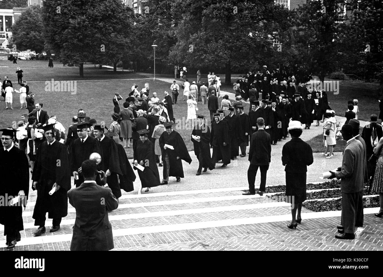 Il giorno d'inizio, una lunga fila di laureati e facoltà che indossano cappucci neri e gli abiti trasportare opuscoli laminati mentre procedono in Shriver Hall, come membri della famiglia di scattare foto sul prato, Johns Hopkins University, Baltimora, Maryland, 11 giugno 1963. Foto Stock