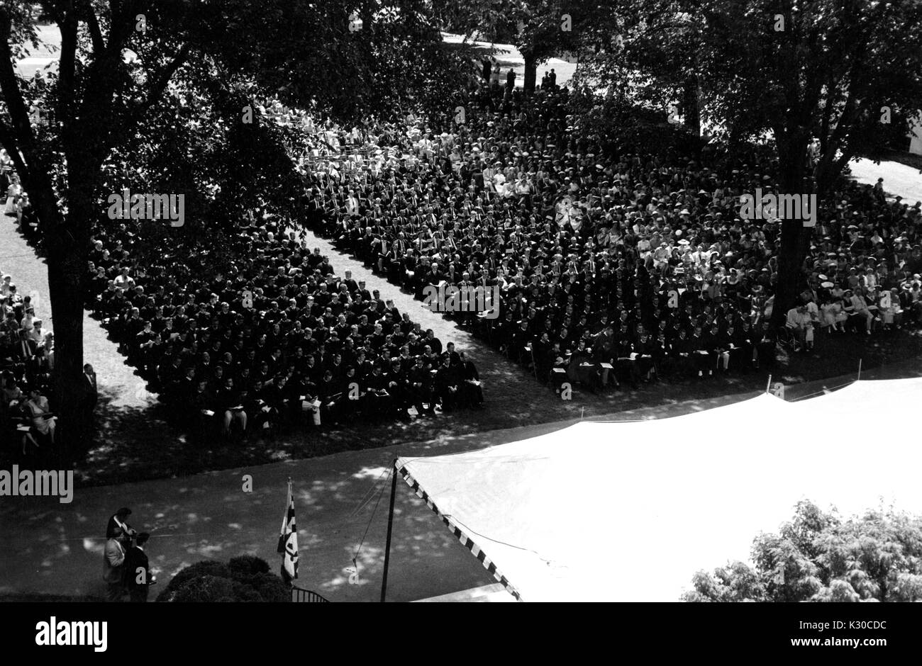Il giorno d'inizio, centinaia di laureati che indossano cappucci neri e gli abiti sit in file ordinate su un ombroso Wyman del quadrangolo durante la cerimonia, guardare gli eventi sul palcoscenico bianco davanti, Johns Hopkins University, Baltimora, Maryland, 11 giugno 1957. Foto Stock
