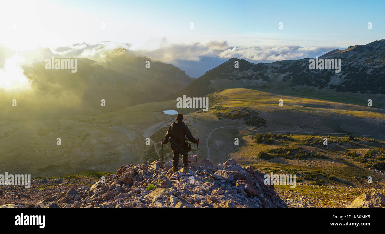 Un escursionista è in piedi sulla montagna con nuvole durante il tramonto/sunrise presso il parco nazionale del monte Rainier, Washington. Foto Stock