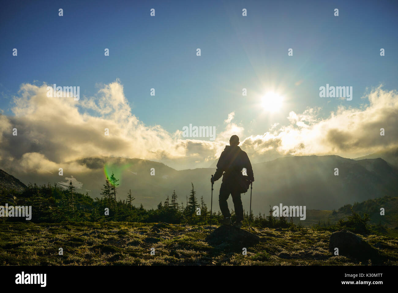 Un escursionista è in piedi sulla montagna con nuvole durante il tramonto/sunrise presso il parco nazionale del monte Rainier, Washington. Foto Stock