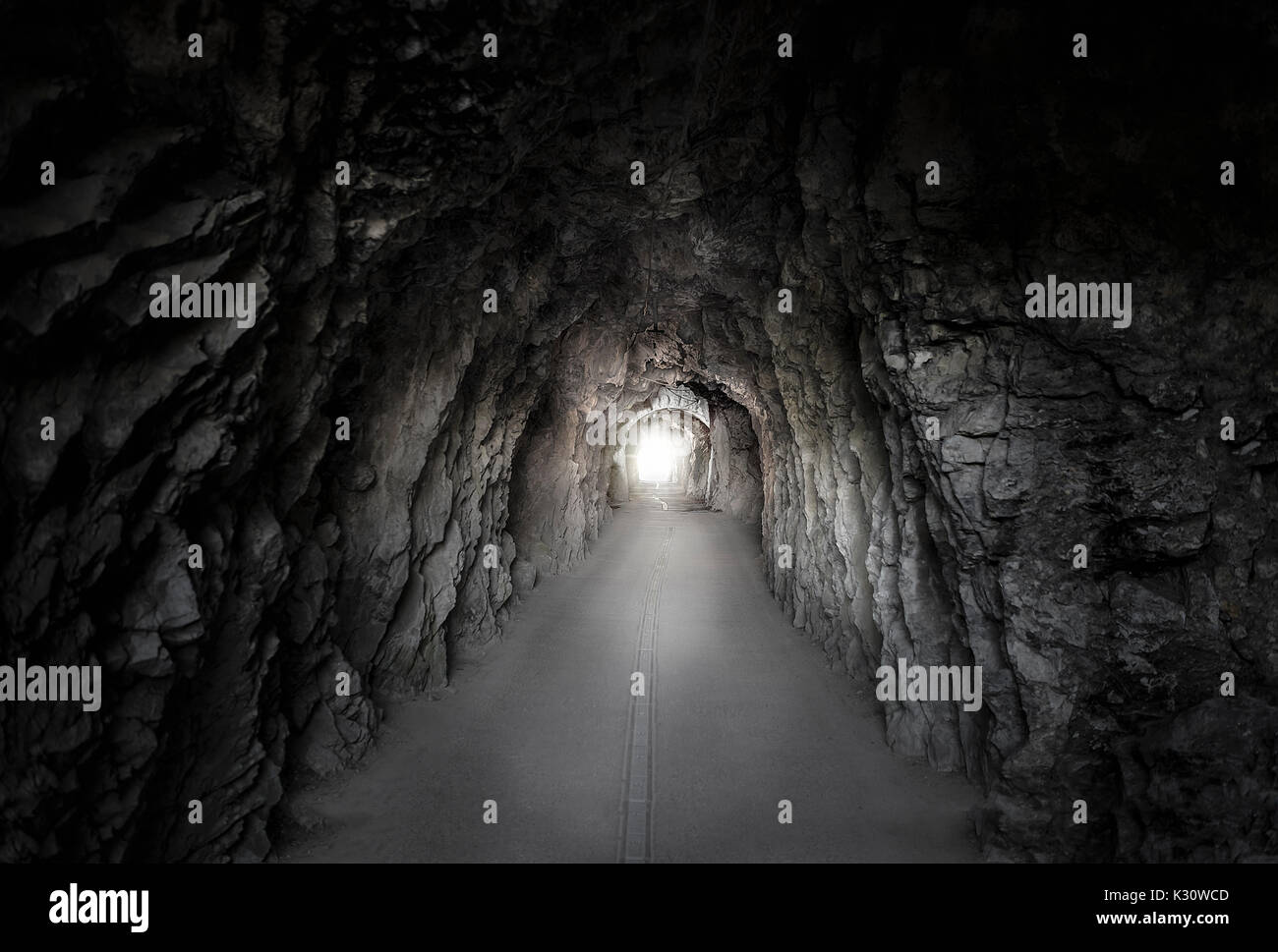 Luce bassa immagine con una strada che passa attraverso un tunnel costruito in una montagna, con muri in pietra e una luce brillante in corrispondenza della sua estremità. galleria situata nel SWI. Foto Stock