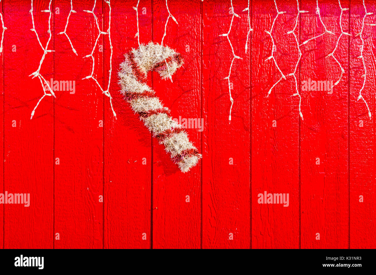 Il bianco e il rosso candy cane contro un rosso parete di legno con le luci di Natale e un sacco di spazio per il vostro messaggio Foto Stock