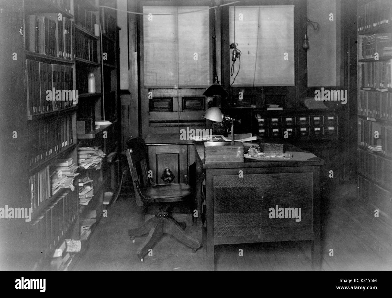 Seppia fotografia della parte interna del secondo piano ufficio del bibliotecario e segretario di reparto all'edificio di chimica del vecchio Campus della Johns Hopkins University, mostrando una scrivania con sedia in centro di scaffali per libri impilati con file e documenti, Baltimore, Maryland, 1924. Foto Stock