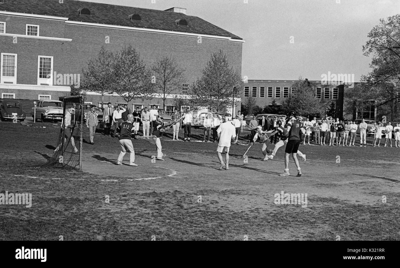 Scala di grigi fotografia di azione durante il maschile di lacrosse pratica presso la Johns Hopkins University, con i giocatori che indossano pantaloncini e magliette come essi corrono verso il traguardo, e una lunga fila di spettatori in piedi presso l'immediata emarginare, Baltimore, Maryland, 1951. Foto Stock