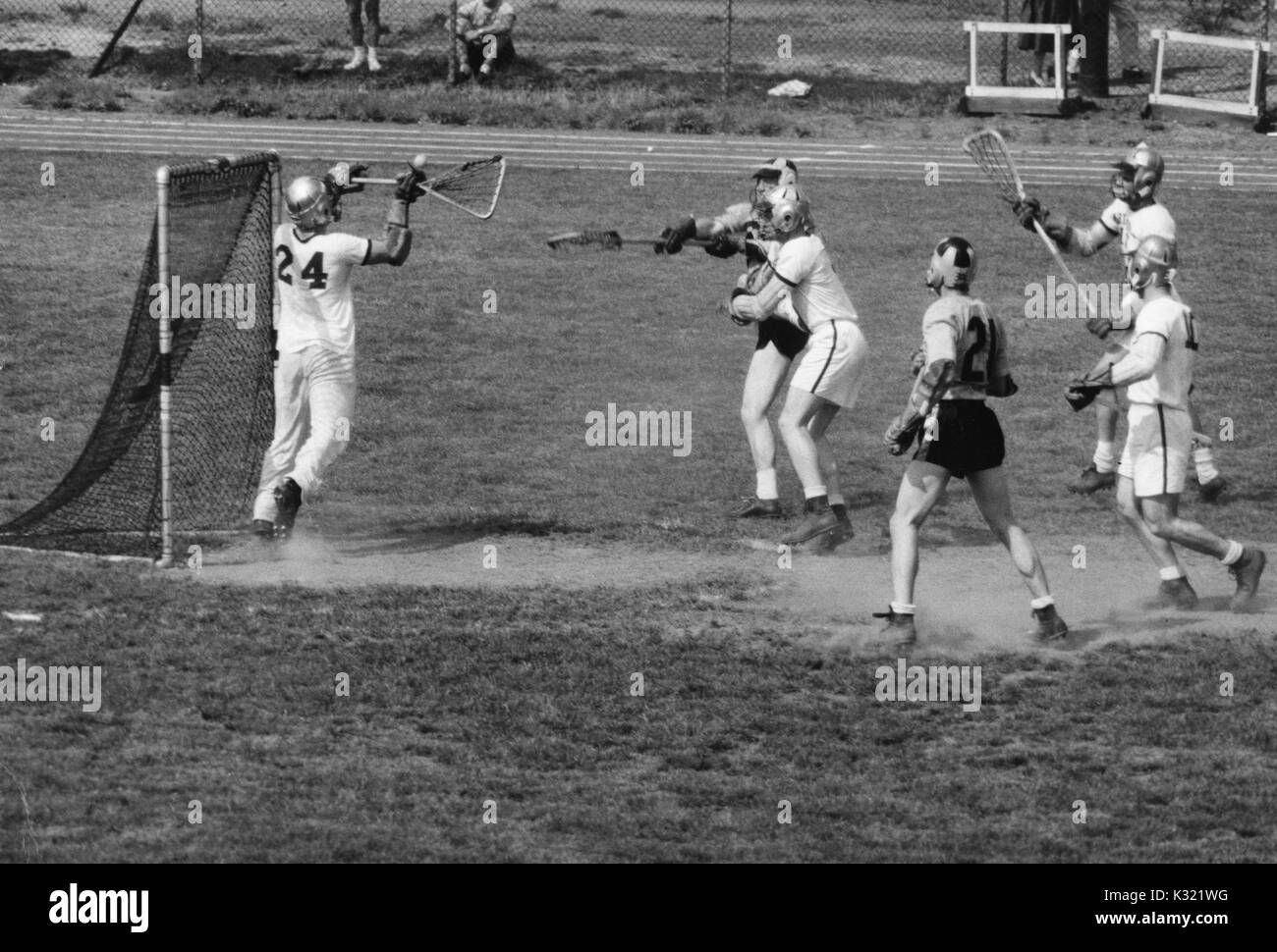 Scala di grigi fotografia d'azione durante un uomo lacrosse match tra la Johns Hopkins University e l'Accademia Militare degli Stati Uniti a West Point, come Micky Webster numero 10 dalla JHU scaglia la sfera dal suo bastone per prendere un colpo mentre esercito difensore e portiere sfida lui e tentare di bloccare il tiro con altri giocatori, tra cui John Jory numero 21 da JHU, seguendo attentamente dietro, Baltimore, Maryland, 27 aprile 1957. Foto Stock