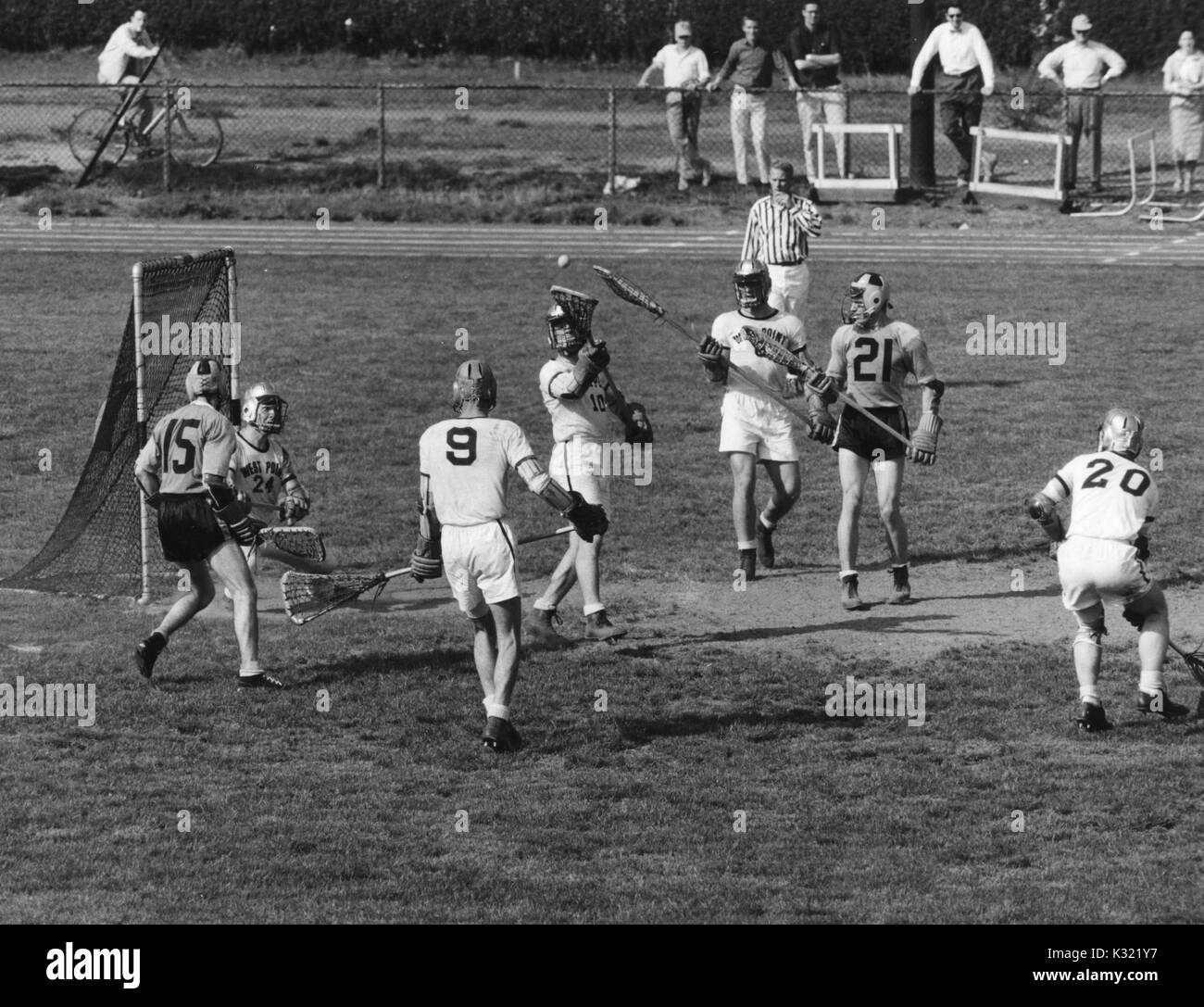 Scala di grigi fotografia d'azione durante un uomo lacrosse match tra la Johns Hopkins University e l'Accademia Militare degli Stati Uniti a West Point, come l'arbitro soffia il suo fischio alla fine di un salvataggio prelevato da un esercito di difesa degli Stati, con il JHU giocatori Billy Morrill numero 15 e John Jory numero 21 circondato da membri della squadra avversaria, Baltimore, Maryland, 27 aprile 1957. Foto Stock