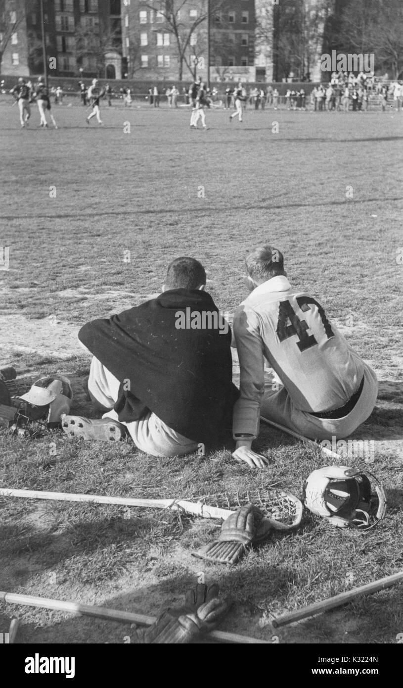 Tonalità seppia candida fotografia di due co-capitani di uomini della squadra di lacrosse alla Johns Hopkins University, Joe Sollers e Byron Forbush, seduti da emarginare sull'erba con spalle, guardando la fine del match con lacrosse bastoni e guanti sparsi dietro di loro, Baltimore, Maryland, Giugno 1951. Foto Stock