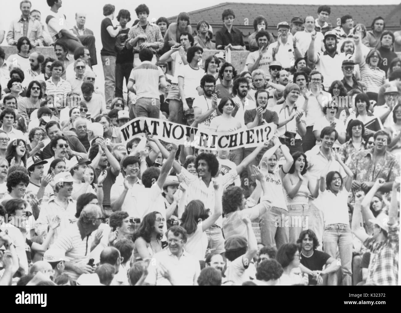 Fotografia in scala di grigi di studenti e appassionati da stand durante un Johns Hopkins University lacrosse corrispondono, mentre tre studenti in possesso di un banner in aria che legge, "che cosa ora Richie!!!?", riferendosi al traguardo di carriera leader Richie Hirsch, Baltimore, Maryland, 1978. Foto Stock