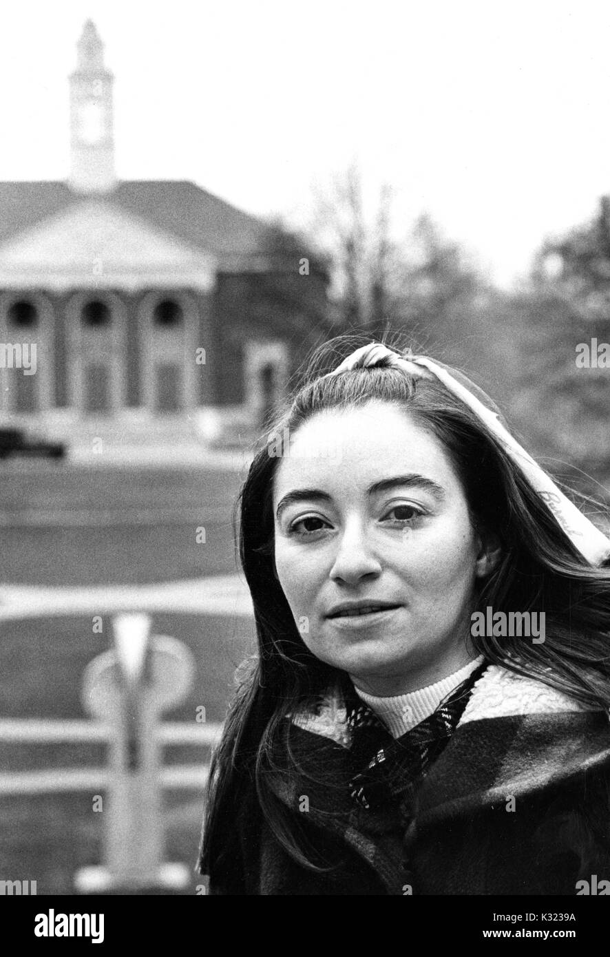 Una femmina di studente laureato alla Johns Hopkins University, indossando il cappotto invernale con archetto in i suoi capelli, comporta per la sua foto sul Breezeway affacciato Wyman Quad, Baltimore, Maryland, 1975. Foto Stock