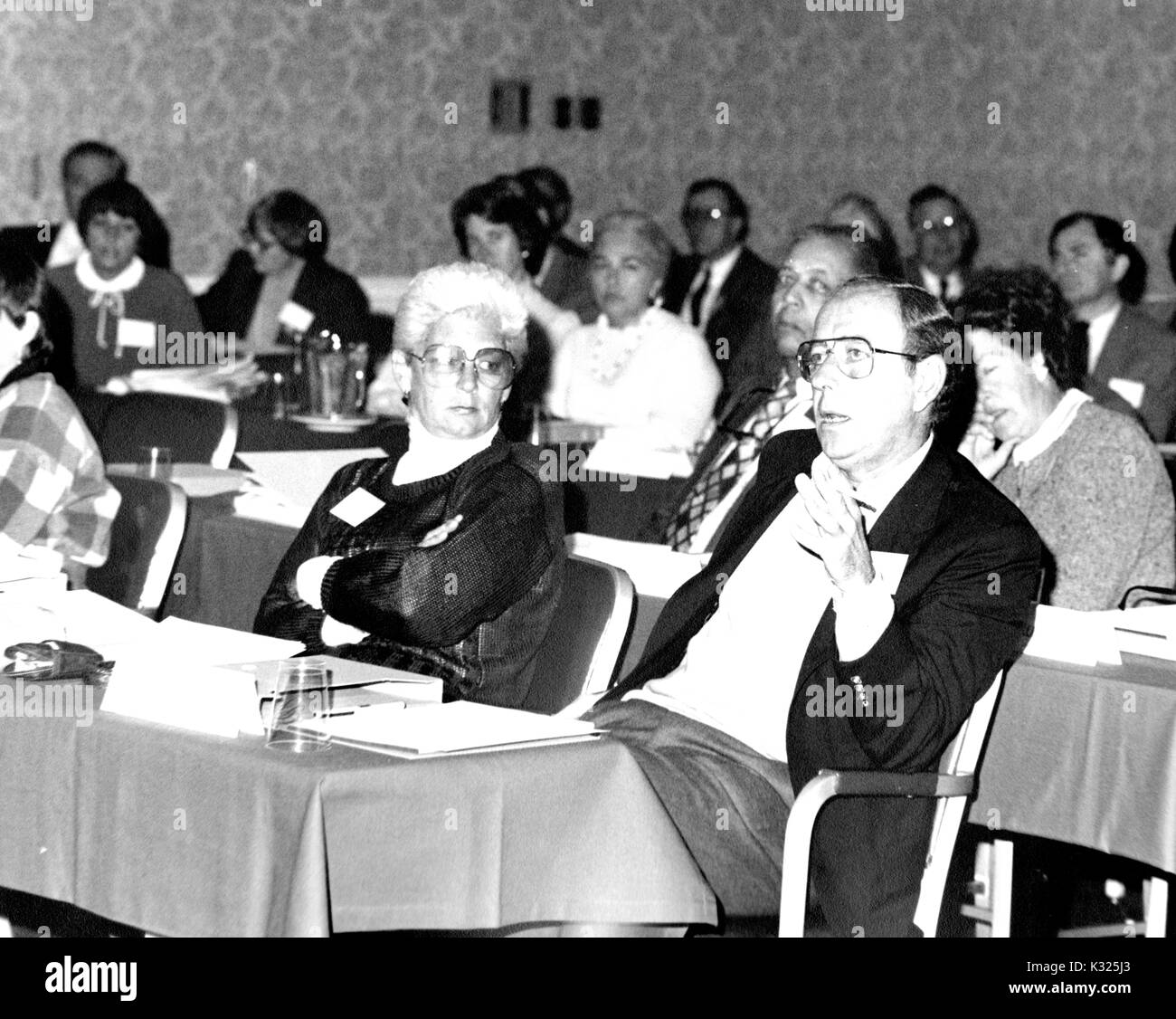 Durante una riunione di campagna per la Johns Hopkins University, i docenti e i membri dello staff sedere ai tavoli in una sala conferenze, mentre Dimitri V d'Arbeloff -- la Terra e Scienze Planetarie scholar presso Johns Hopkins -- si siede indietro nella sua sedia, indossa una tuta e occhiali, proponendo un movimento verso la testa della camera, Baltimore, Maryland, 1983. Foto Stock