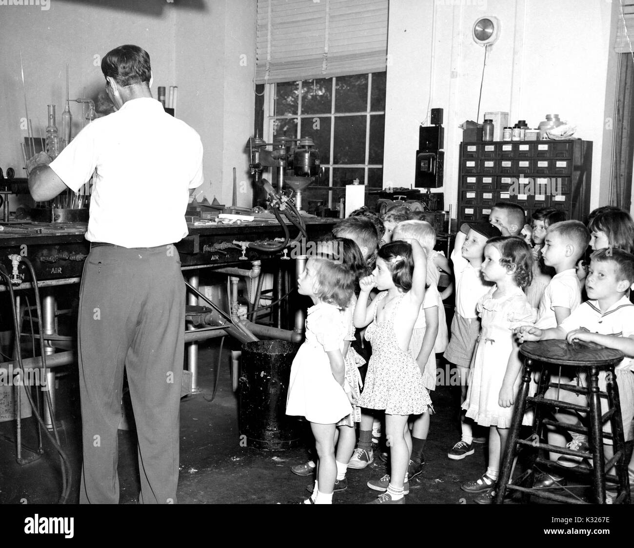 Gli studenti della scuola materna di classe di una dimostrazione elementare Scuola di Johns Hopkins University stare a guardare di fascino mentre un soffiatore di vetro opere su un pezzo con la sua schiena girata, durante un campo estivo viaggio a un vetro soffiando studio, luglio 1950. Foto Stock