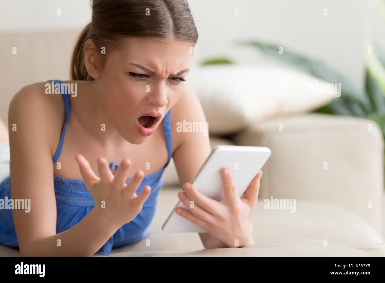 Scioccato giovane donna con tavoletta digitale in casa Foto Stock