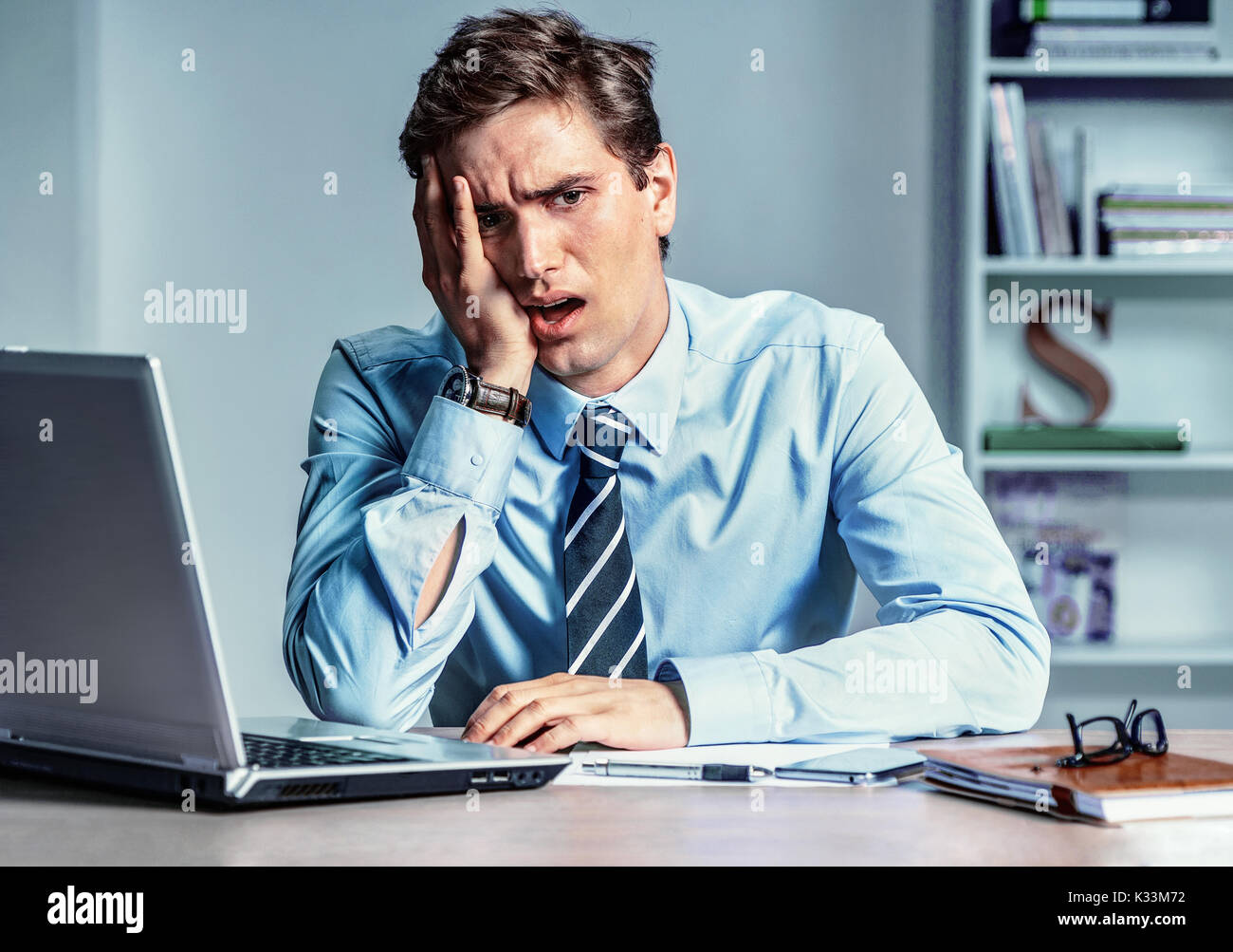 Addolorato giovane uomo mantiene la sua testa con la mano. Imprenditore moderno sul luogo di lavoro, depressione e il concetto di crisi Foto Stock