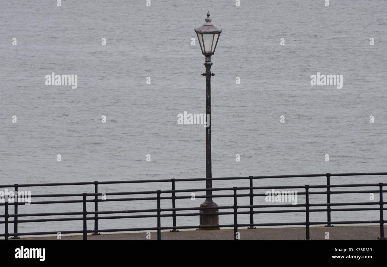 Un antico lampione e ringhiere su un opaco, grigio, giorno nuvoloso sul lungomare a Southsea. Southsea. Portsmouth, Hampshire, Regno Unito. Foto Stock
