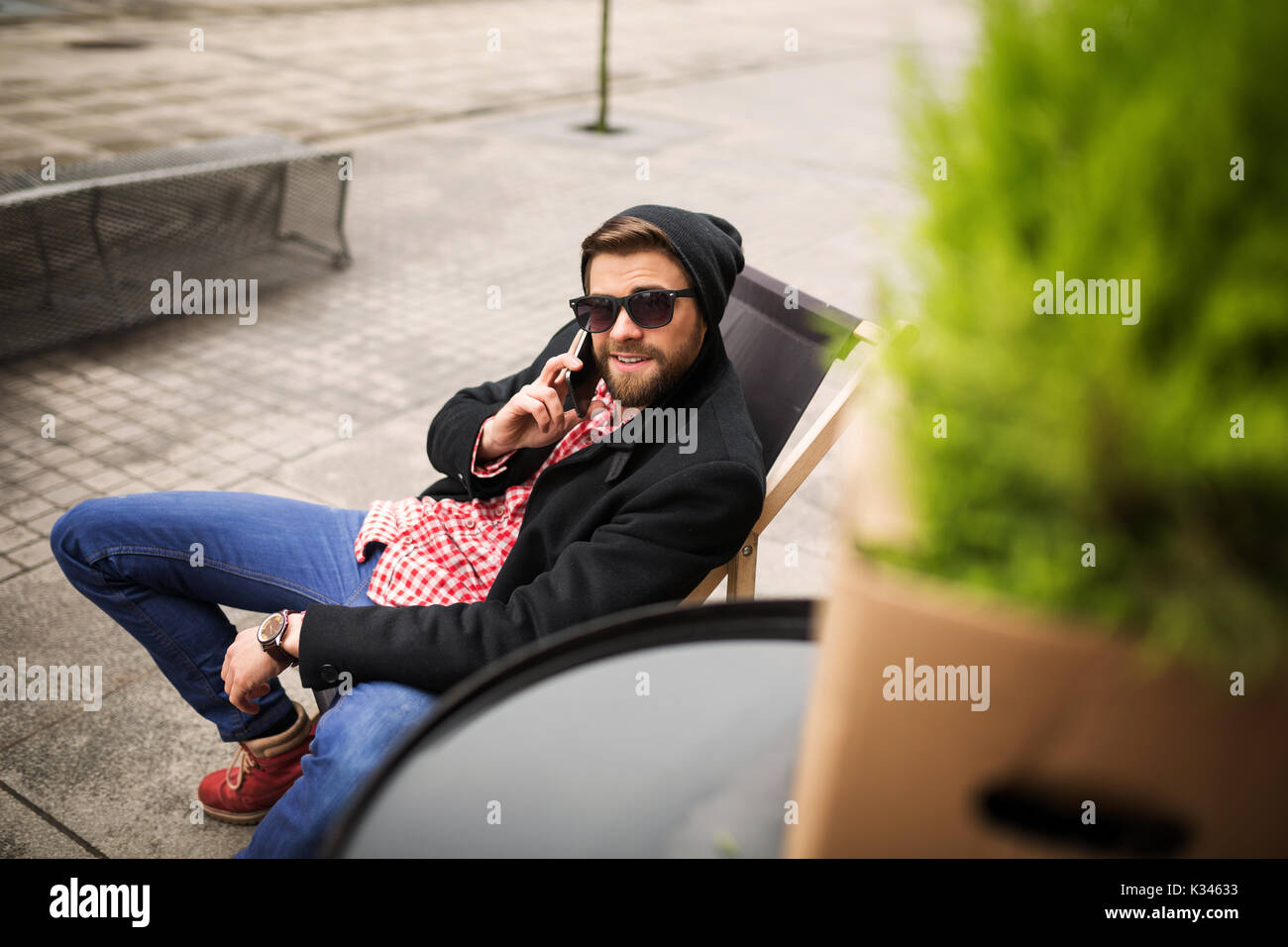 La foto di un giovane uomo seduto sulla sedia a sdraio e parlare al cellulare. Foto Stock