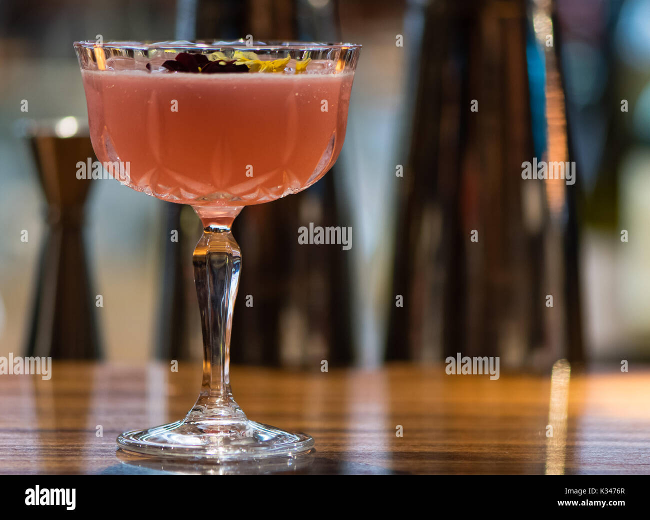Cocktail rosa guarnito con fiori in vetro di Margarita. La bevanda alcolica nel bicchiere sul banco in legno della barra Foto Stock