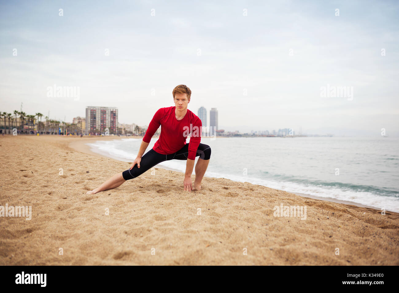 La foto di un giovane uomo sportivo che si allunga sulla spiaggia. Foto Stock