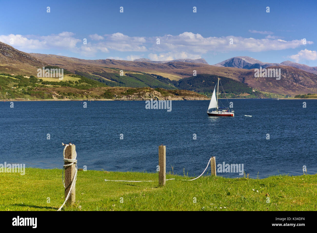 Sailing yacht in mare con la gamma della montagna in background e verde riva erbosa in primo piano, Ullapool, Wester Ross, Scozia Foto Stock