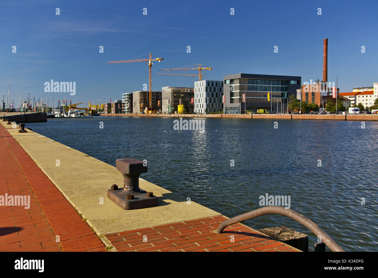 La vista del porto con mattoni rossi quay e bollard in primo piano e di edifici per uffici e siti di costruzione in background, Bremerhaven, Germania Foto Stock