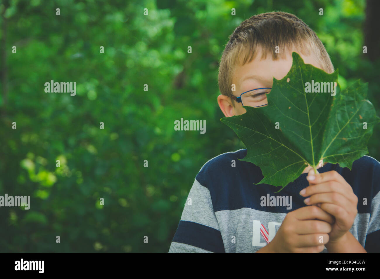 Un giovane ragazzo detiene una foglia verde nella parte anteriore del suo volto. Foto Stock