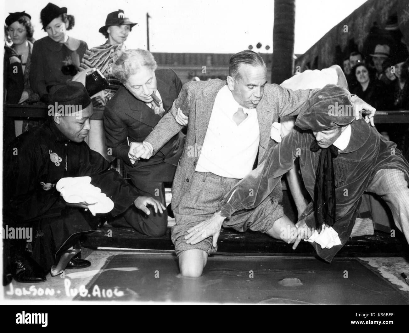 Al Jolson rendendo knee-stampe in calcestruzzo al di fuori del Sid Grauman's Theare cinese. Sid Grauman è tenuta su Jolson il braccio destro. Foto Stock