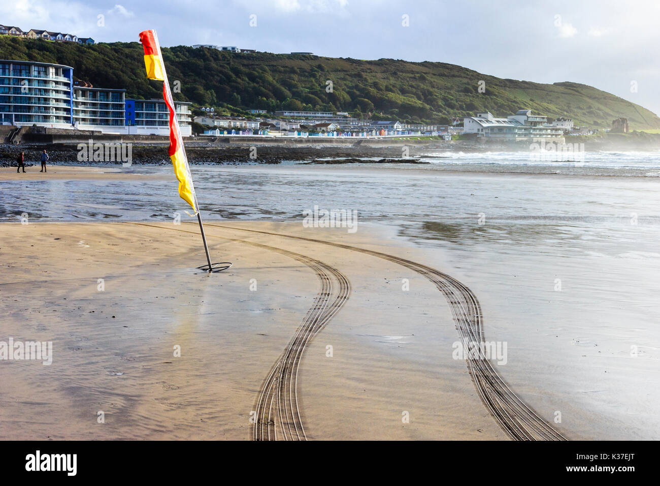 Rosso e giallo di avvertimento bandiera e tracce di pneumatici da RNLI veicolo sulla spiaggia di sabbia con la bassa marea, Condino, Devon, Inghilterra, Regno Unito Foto Stock