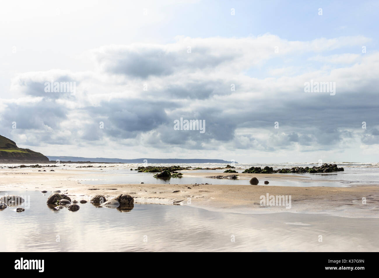Bassa angolazione della spiaggia sabbiosa a Condino, Devon, Inghilterra, Regno Unito, con la bassa marea con riflessi del cielo e delle nubi in piscine di roccia Foto Stock