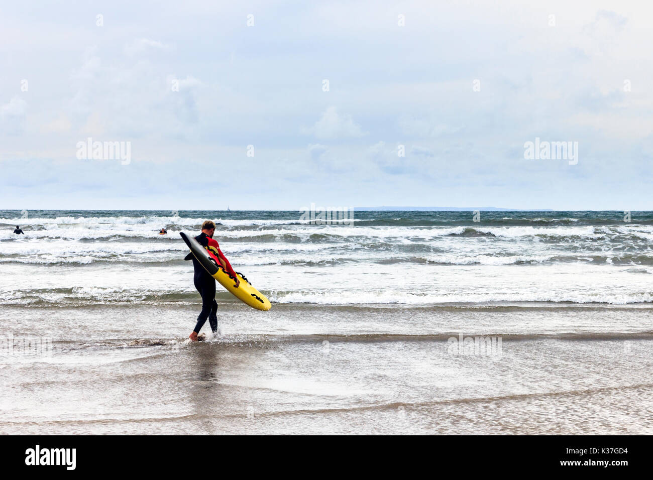 Un singolo surfista maschio portando la sua giallo e nero tavola da surf al mare a Condino, Devon, Inghilterra, Regno Unito Foto Stock
