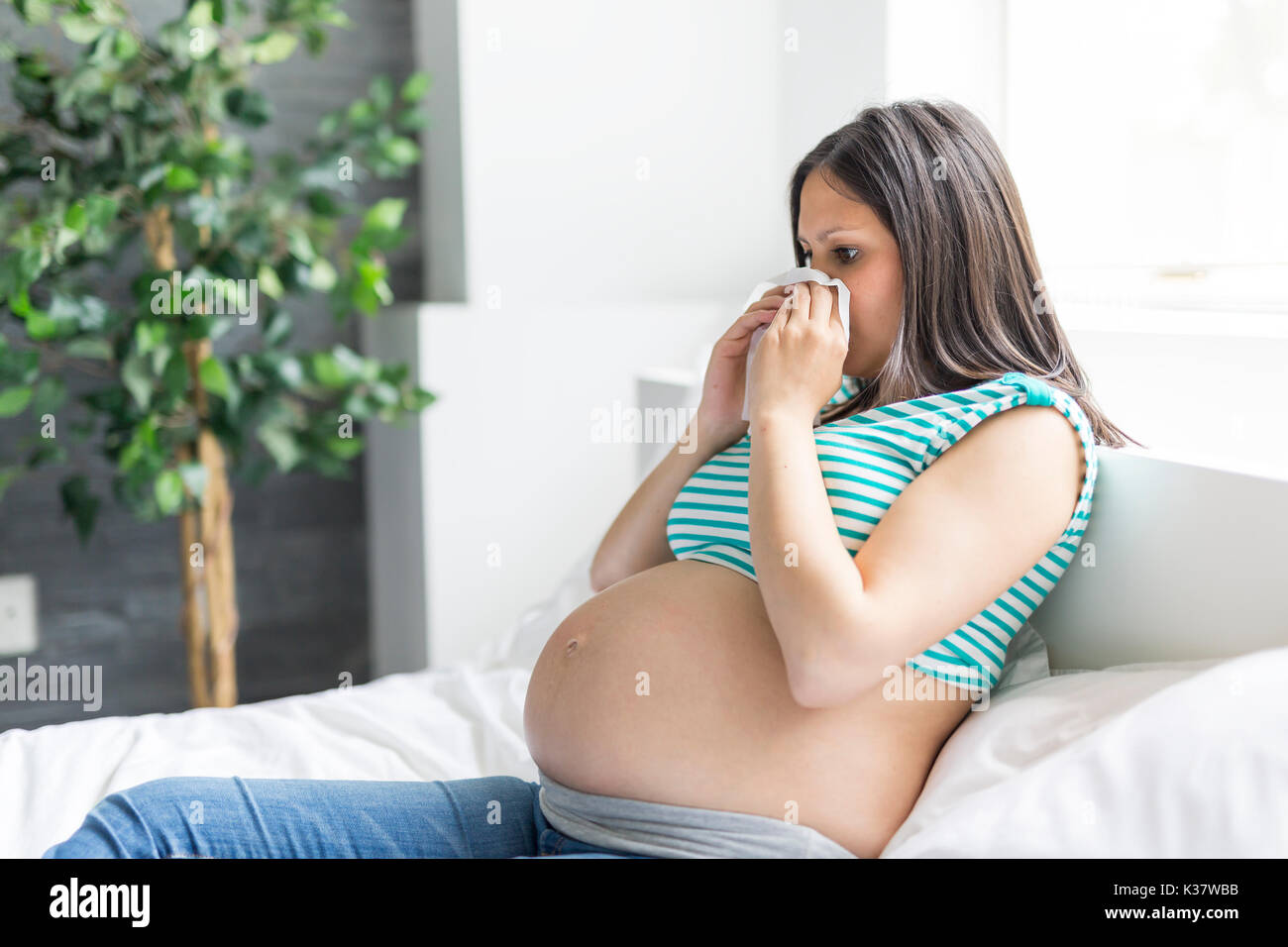 Donna incinta in posa mentre giaceva su un letto di casa con flu Foto Stock