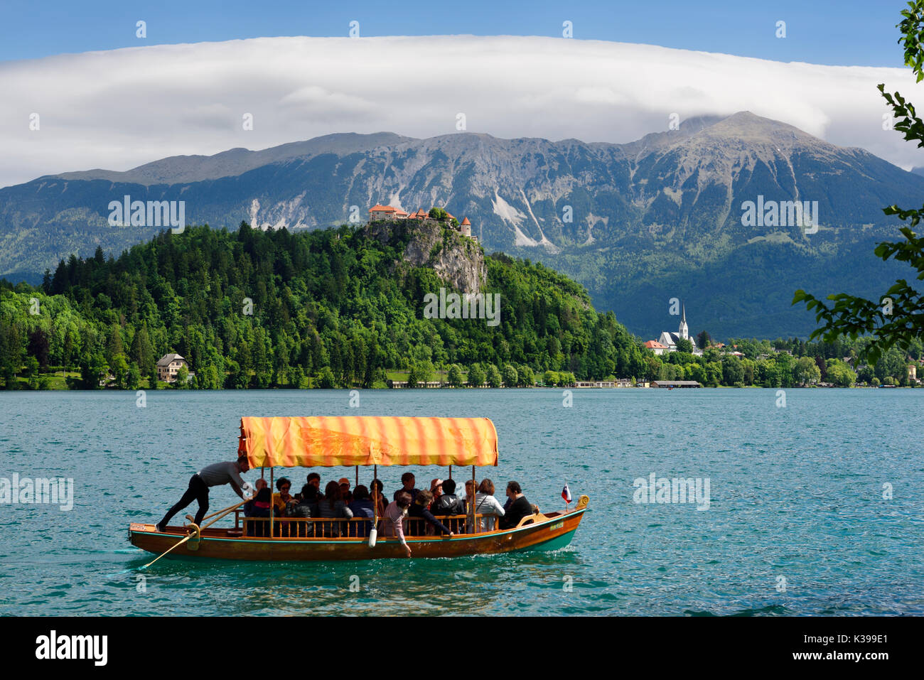 Tradizionale barca Pletna con tettoia colorati sul lago di Bled con il castello di Bled sulla scogliera e la chiesa di St Martin Sol massiccia delle Caravanche Slovenia Foto Stock
