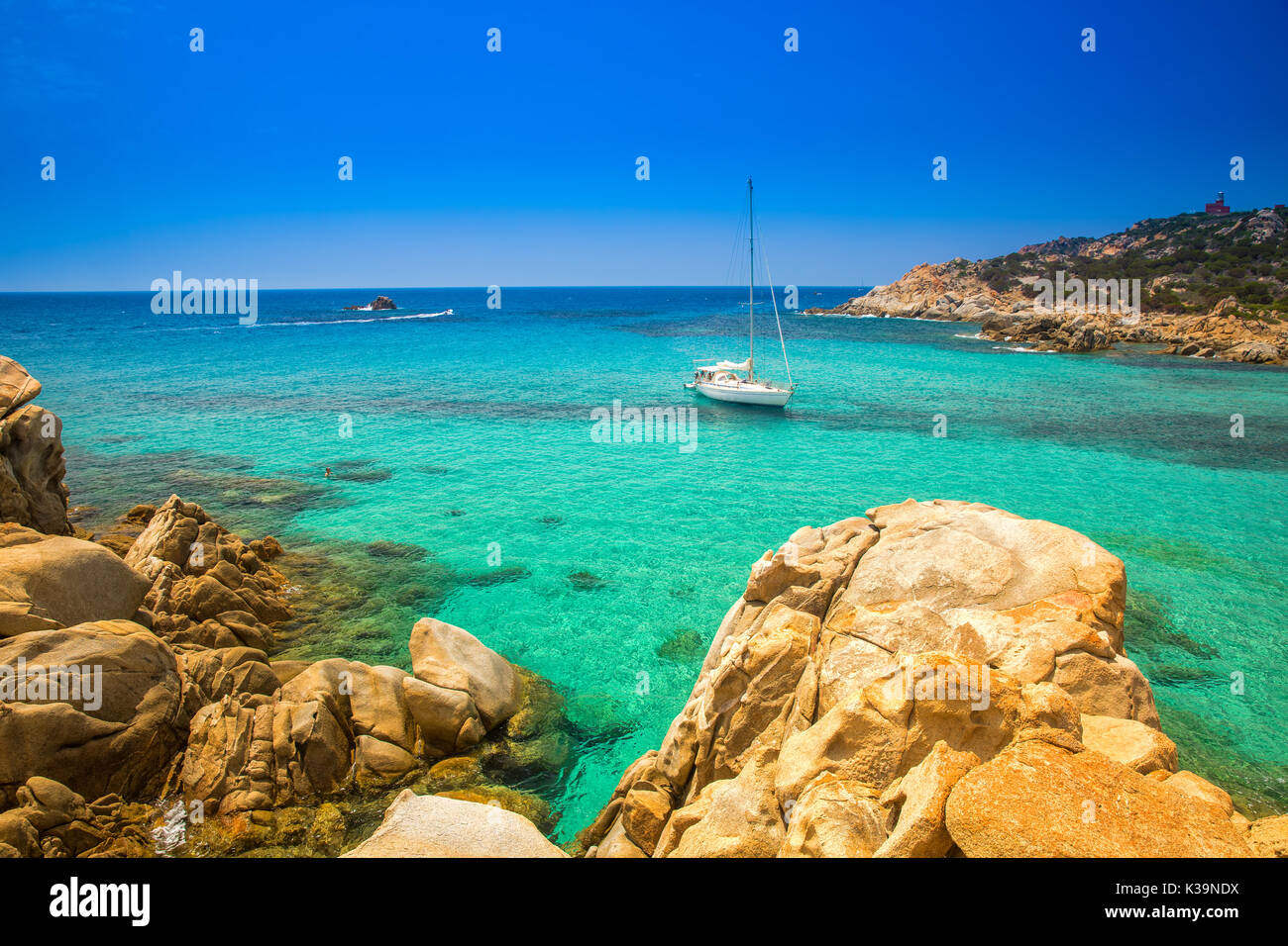Yacht sulla spiaggia di Chia con pietre di colore rosso e azzurro acqua chiara. La Sardegna è la seconda isola più grande del Mediterraneo. Foto Stock
