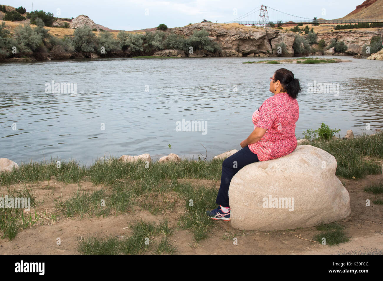 Una donna seduta su una pietra presso la riva del fiume Bighorn, Themopolis, WY Foto Stock