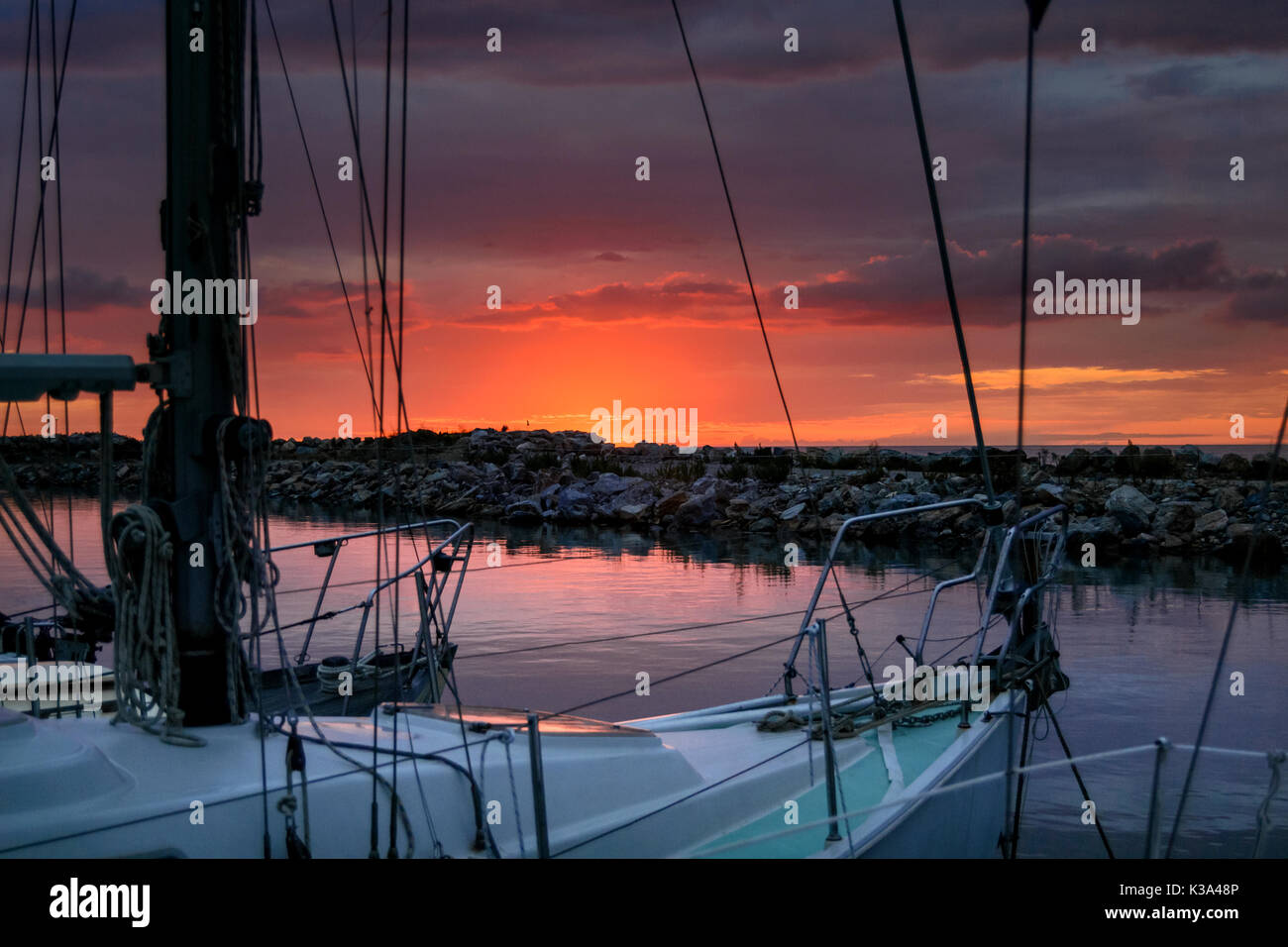 splendido tramonto sul mare, dietro le scogliere, in una tranquilla serata estiva rilassante nel porto tra le barche a vela Foto Stock