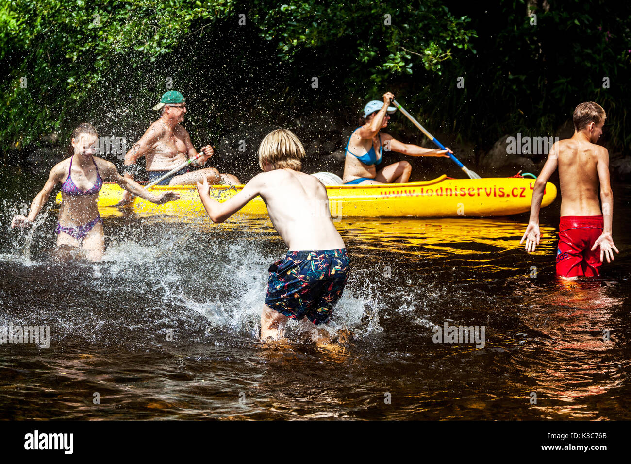 Gli adolescenti gli spruzzi di acqua in corrispondenza di ogni altro nel fiume Otava, passando attorno gli anziani in una canoa, Repubblica Ceca Foto Stock