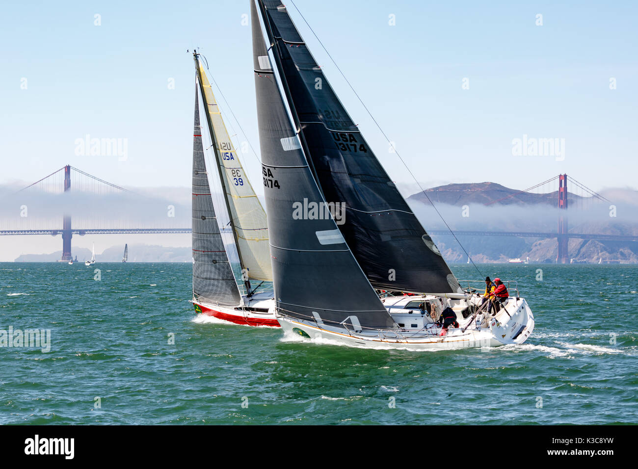 Una barca a vela bianca supera uno rosso in gara fino al Golden Gate Bridge e sul retro Foto Stock