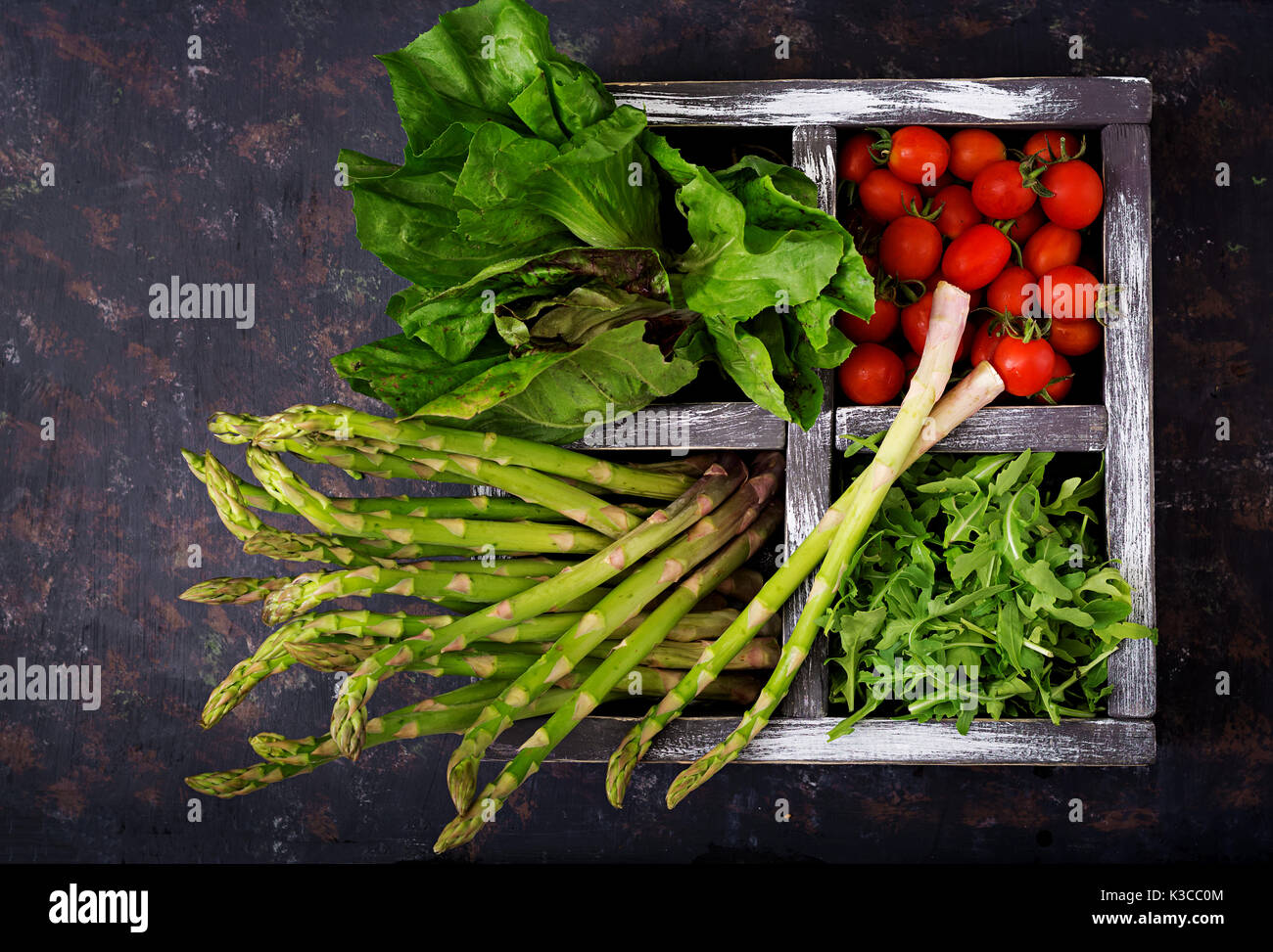 Asparagi freschi, pomodoro. la rucola e lattuga in cassetta di legno su sfondo scuro Foto Stock
