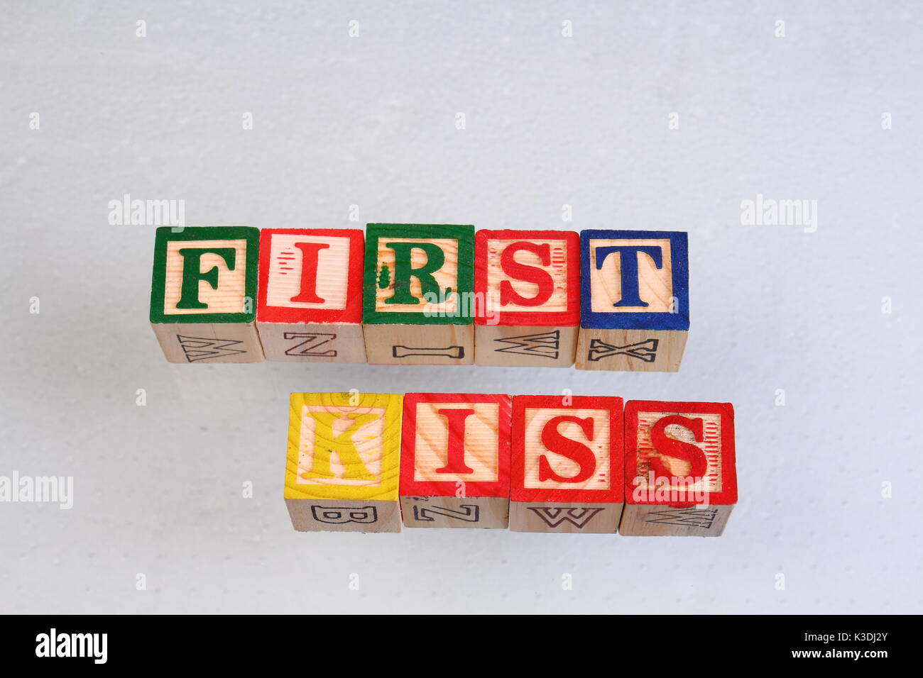 Il termine primo bacio visualizzate visivamente su uno sfondo bianco utilizzando in legno colorato blocchi giocattolo in formato paesaggio con spazio di copia Foto Stock