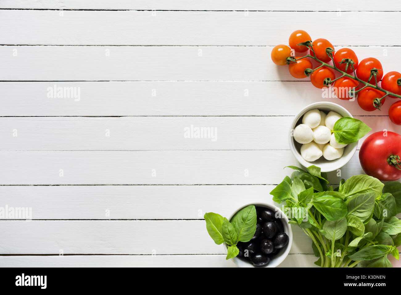 I cibi freschi ingredienti per cucina italiana. mazzetto di basilico verde, olive nere, mozzarella e pomodoro in bianco sullo sfondo di legno. top view wi Foto Stock