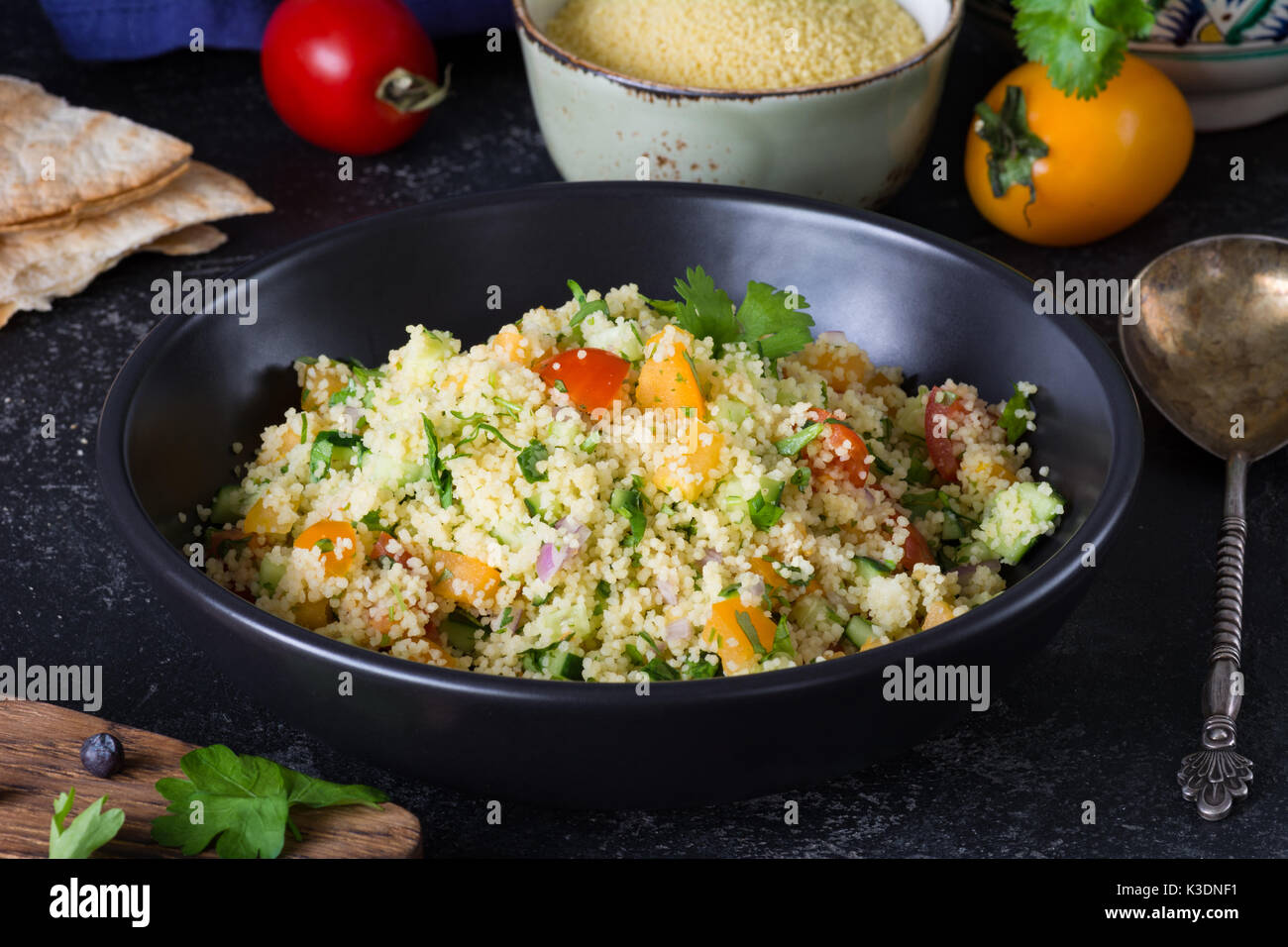 Arabo libanese cucina: una sana deliziosa insalata di cous cous, verdure fresche e verdi chiamato tabulé in nero ciotola. autentica cucina Foto Stock
