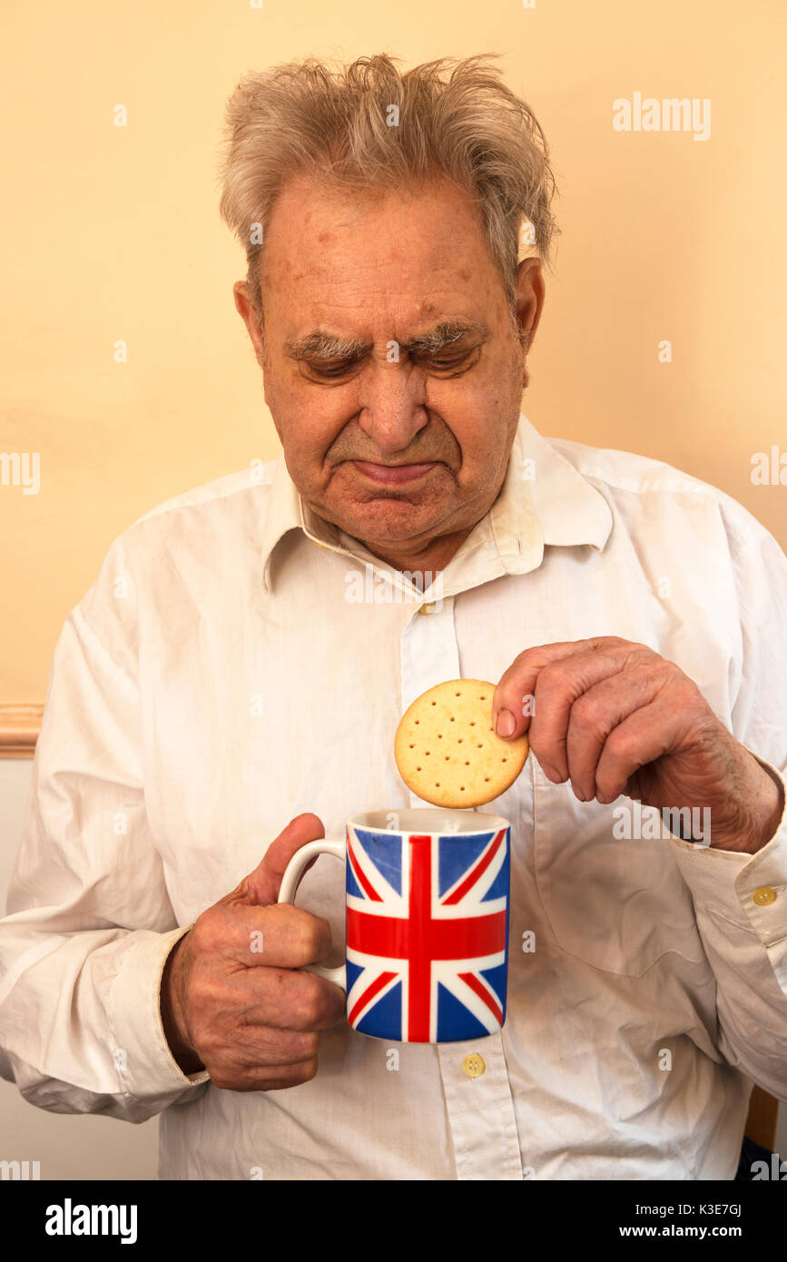 Uomo anziano con due tipo di diabete mangiando un biscotto con una tazza di tè Foto Stock